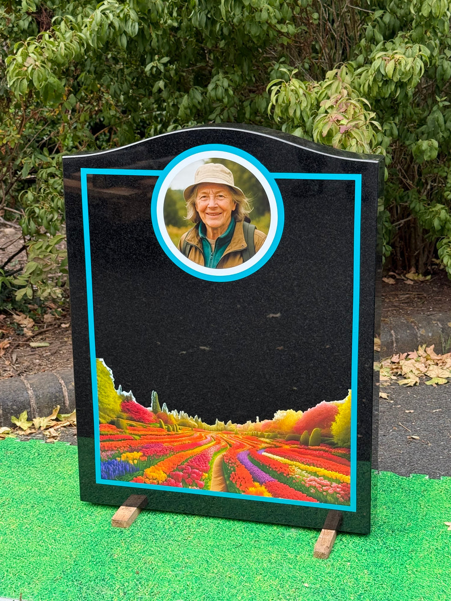 Black granite memorial featuring a circular portrait and colourful garden scene